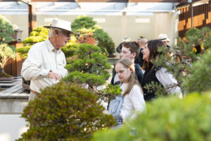A young woman with a Down Syndrome, her brother and mother listen to a man talking about the bonsai tree they are looking at
