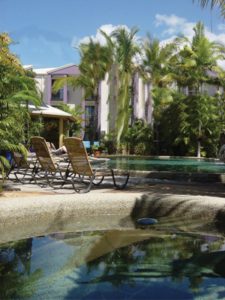 A beautiful tropical pool with some sun lounges, surrounding them is greenery including lots of ferns