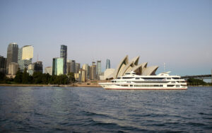Boat passing Opera House with city in the background 300x188